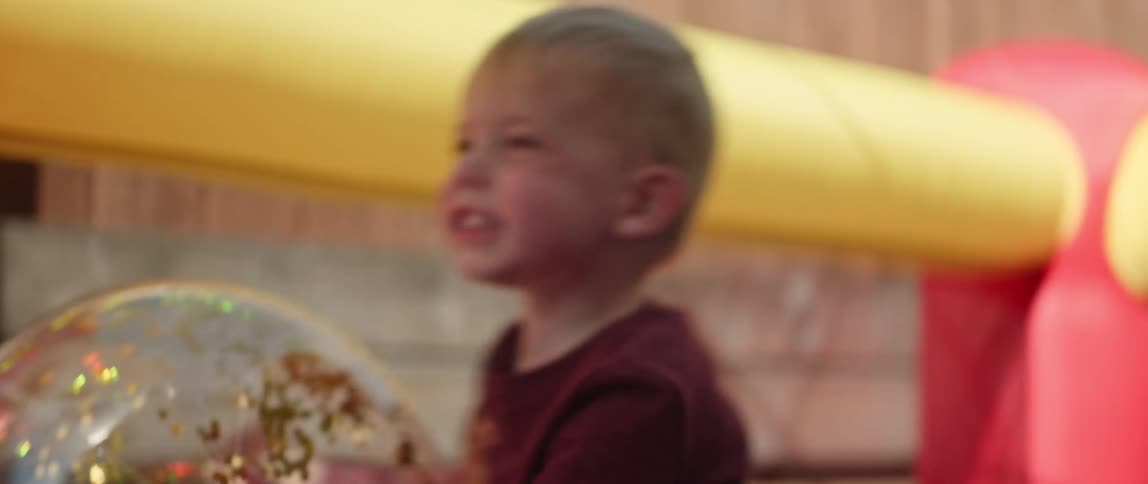A little boy is in a playroom holding a big ball smiling and laughing as he plays