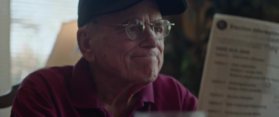 An elderly man is sitting down and is reading something