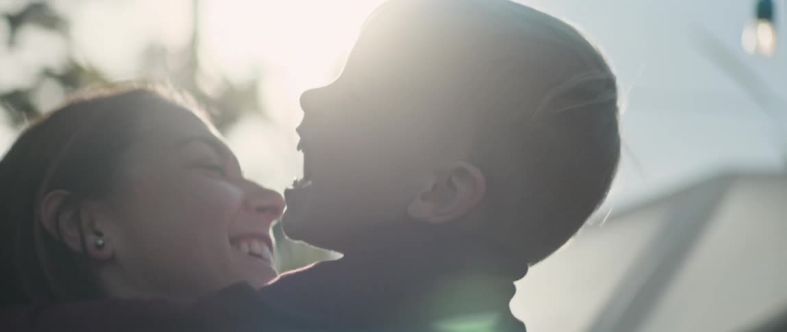 Mother and toddler boy hugging smiling laughing standing outdoors with sun shining