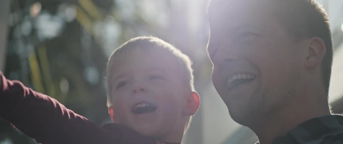 Father holding toddler son laughing under sunlight