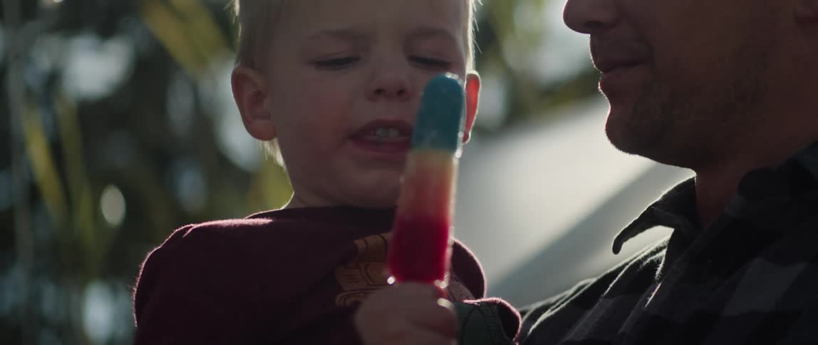 A father holds his son in his arms while the boy eats a popsicle