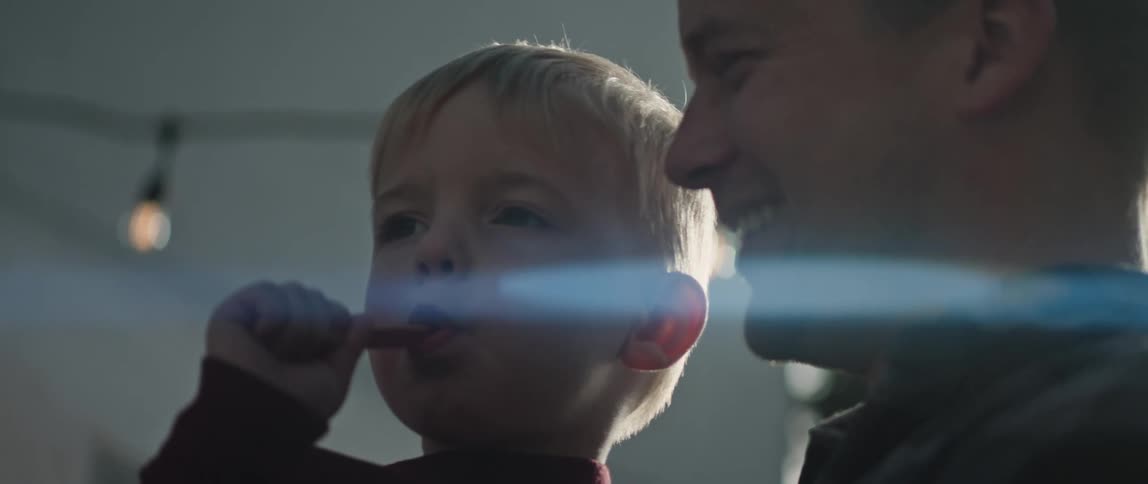 Son sucks on popsicle stick while father holds and kisses the child