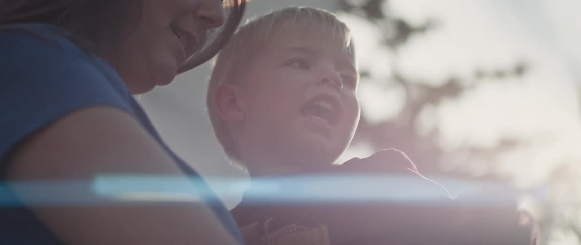 Mother in blue t shirt holds son pointing and talking to his mom under shining sun