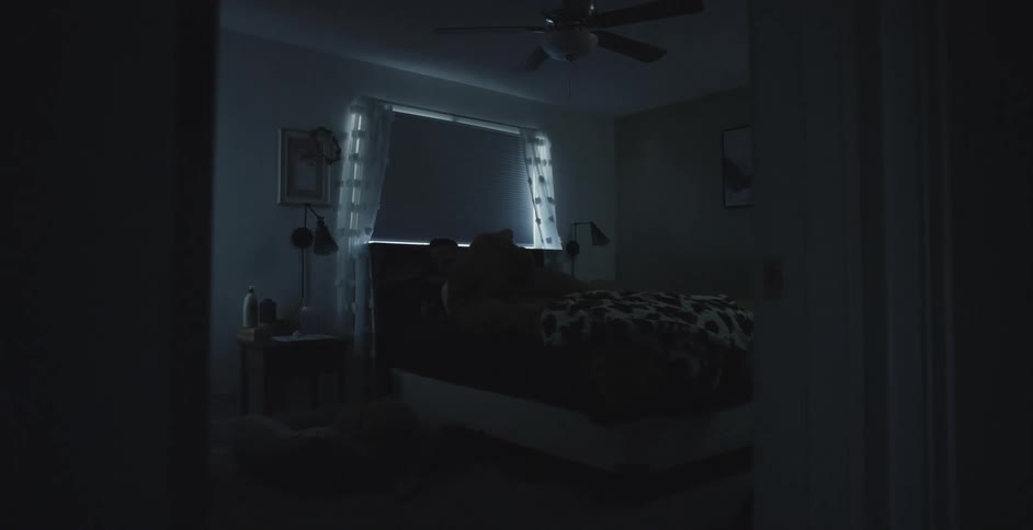 A sleeping man wakes up and moves the blankets covering him and gets out of bed and walks out of the bedroom