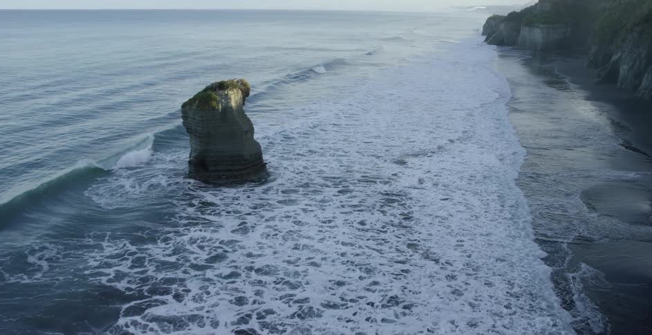 An aerial view of waves rolling in to the shore surrounded by cliffs