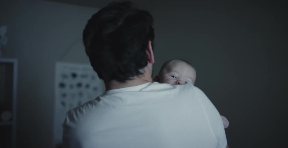 Father with beard and white shirt rocks newborn baby in his arms