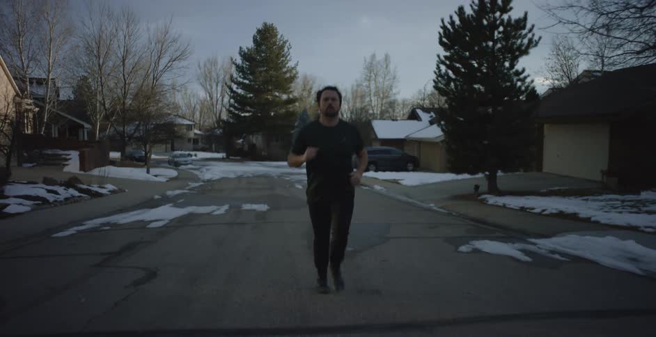 A man is running down a neighborhood street on a winter day as the snow on the ground is melting