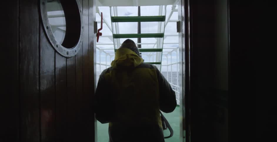 A man is walks out of a dark hall carrying a camera
