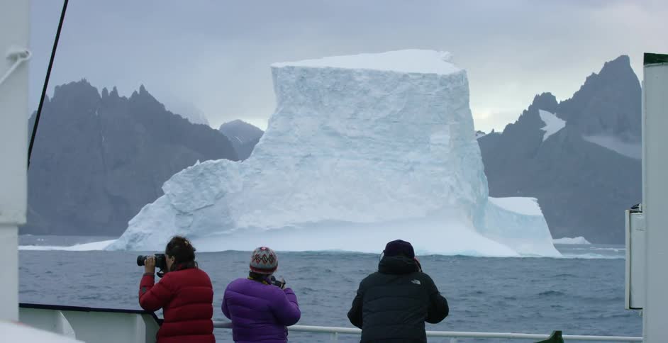 People on a boat are looking at and taking pictures of an iceberg