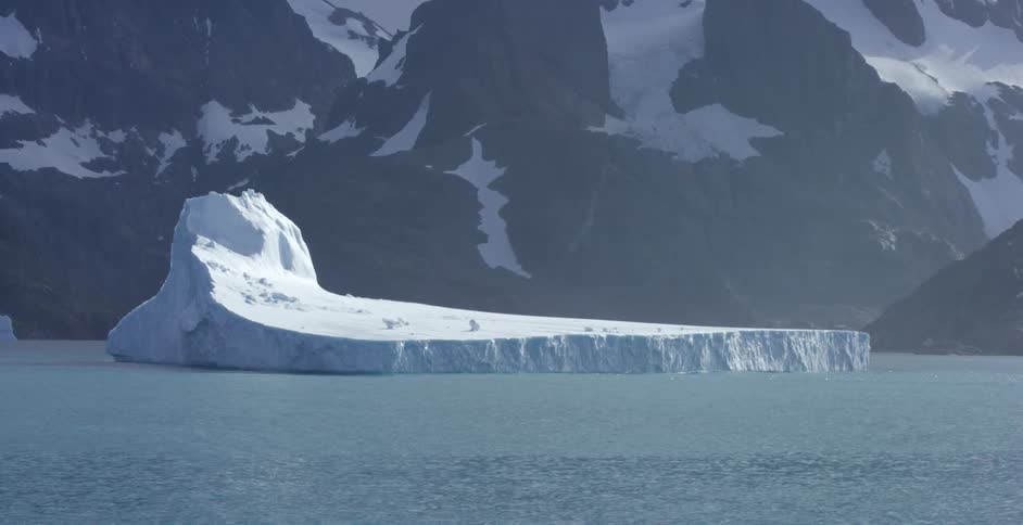 An iceberg floats off the coastline at the base of a mountain range