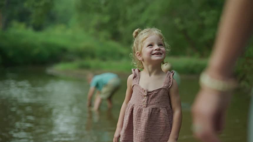 A young girl smiles while outside in a creek with some other children