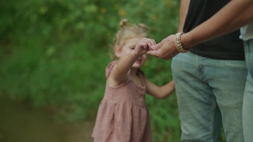 Little girl standing in lake water hands a found object to mom