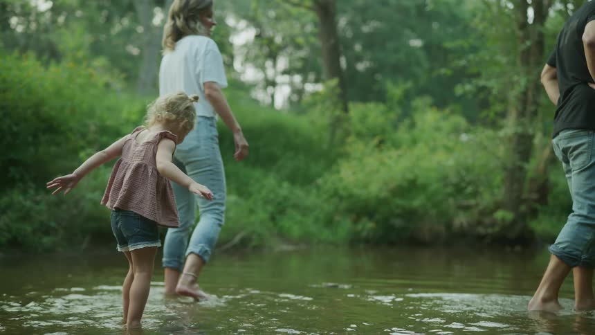 Mother daughter and father walk in river near the green forest