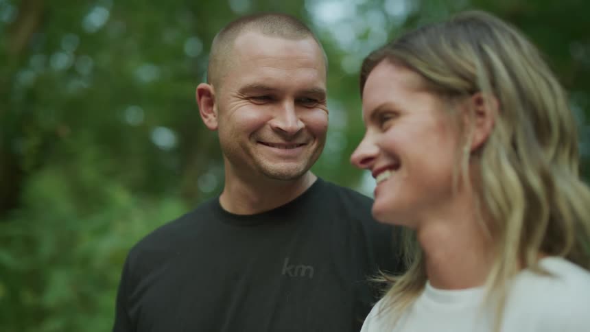 Man and woman standing together outside laughing and smiling at one another before looking up