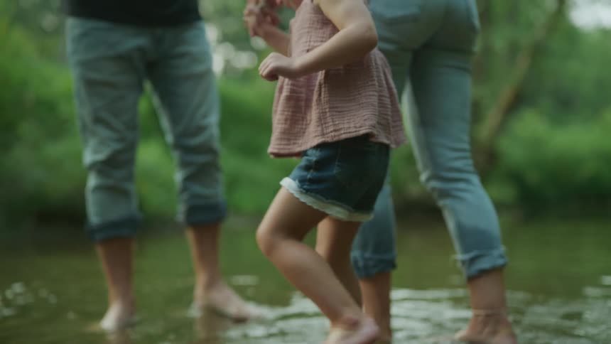 Two adults walk through the water in nature with a child