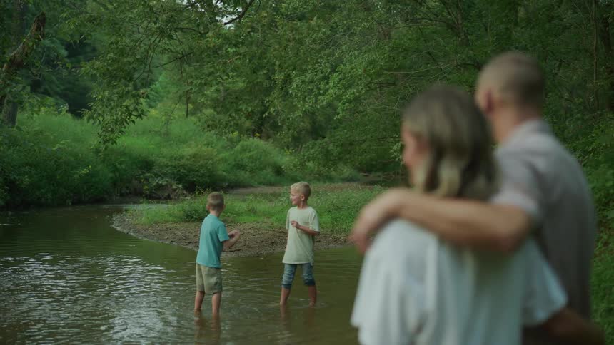 Father and mother look at two sons in the river