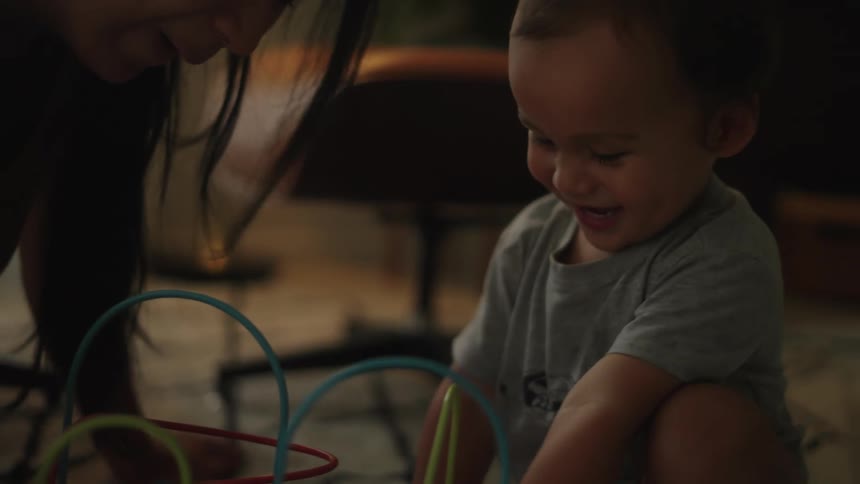 A mother plays with her son on the floor as he laughs and smiles in excitement