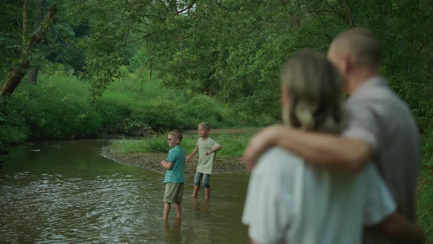 Family spending time at the lake two boys skipping rocks in the lake while mom and dad look on