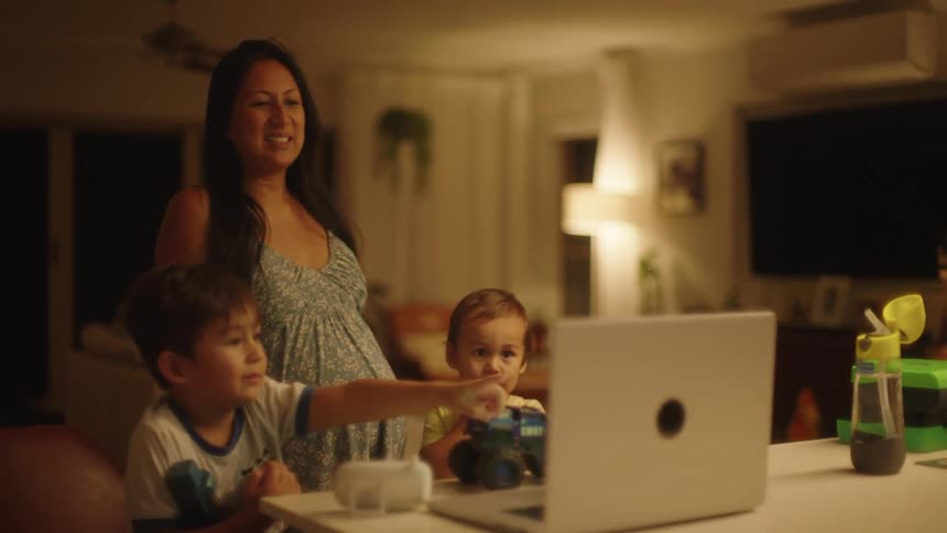 Mother with white dress and two sons look at laptop on the table