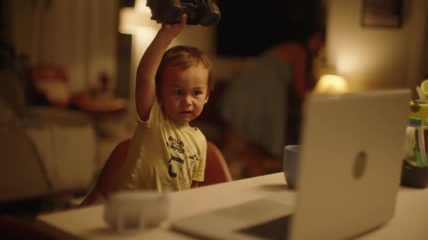 A child waves a toy car in front of the laptop