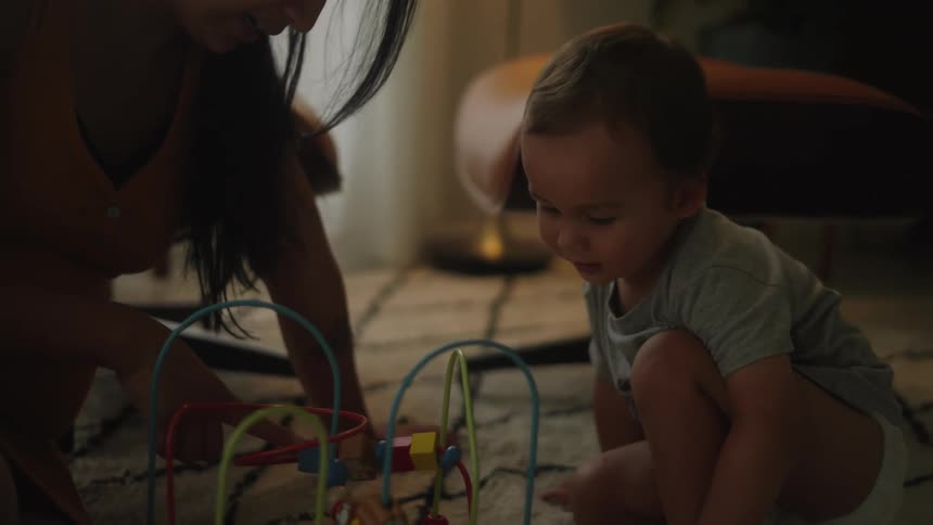 A little boy and his mother play with a toy on the floor as the boy smiles and laughs