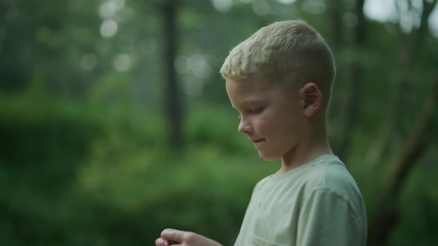 Blonde boy with green shirt stands in the river next to woods