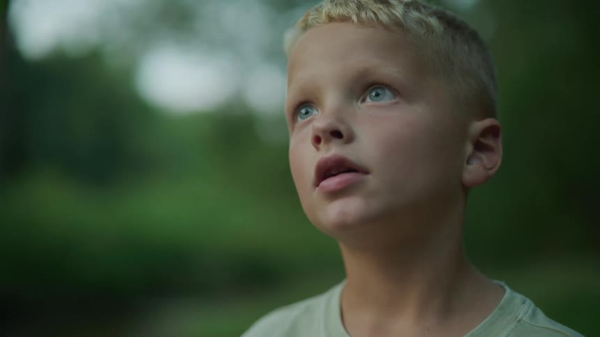A young boy standing looking upward with a sad face taking a deep breath