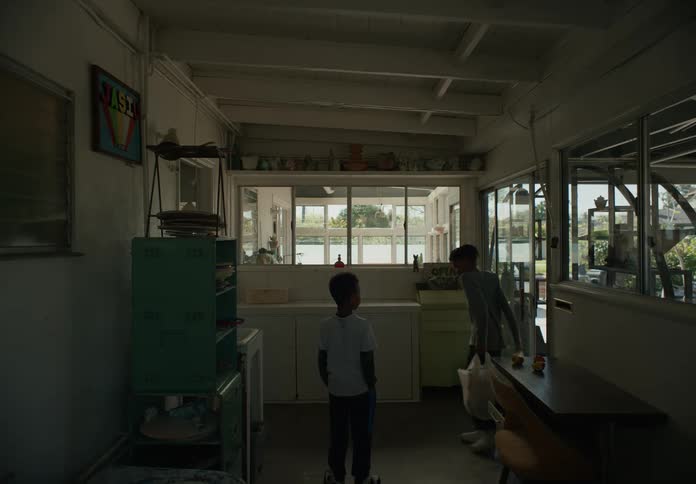 Boys with undershirts and dreadlocks enter kitchen carrying bags