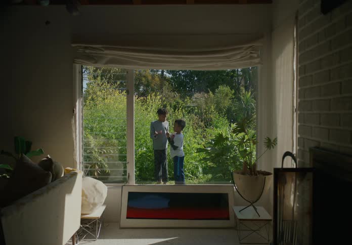 Brothers playing outside with a stick and fighting each other in front of a large window