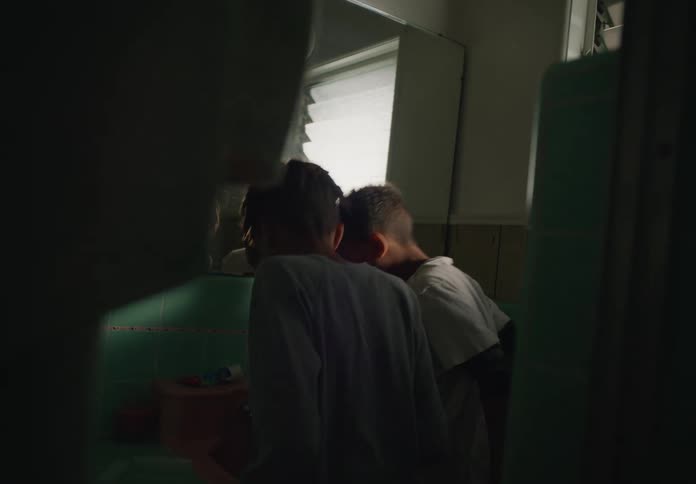 Two young brothers in bathroom over sink spitting water into sink probably brushing teeth