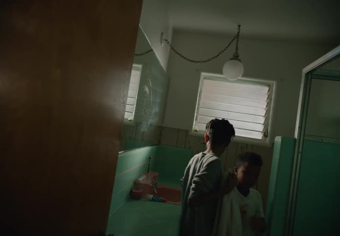 Brothers in a bathroom while the older one helps the younger one dry his face
