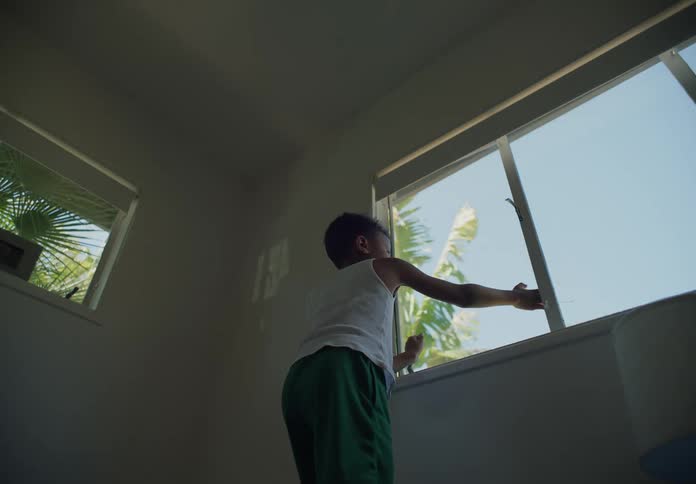 A young boy standing in front of a window looking out and looking back
