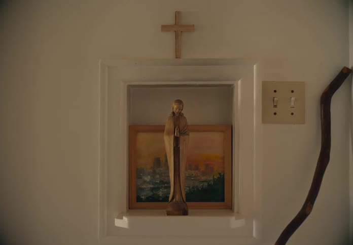 A statue of a woman praying is on a shelf in front of a painting with a wooden cross sitting on top of the frame