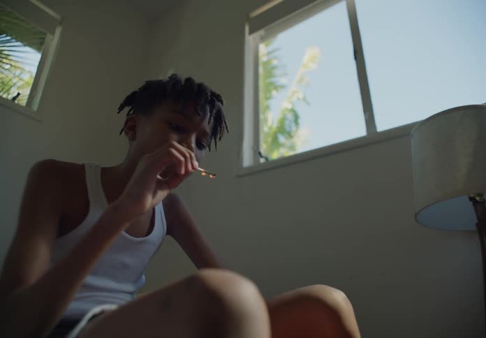 A young boy sitting in his room with a lit match in his hand while he blows out the flame