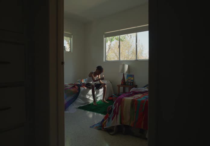 Youth sits on one of two beds and strikes a match then examines it