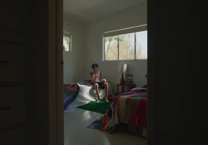 A young boy sits on his bed and lights a match when his younger brother comes in to the room and stands up on the other bed to watch him