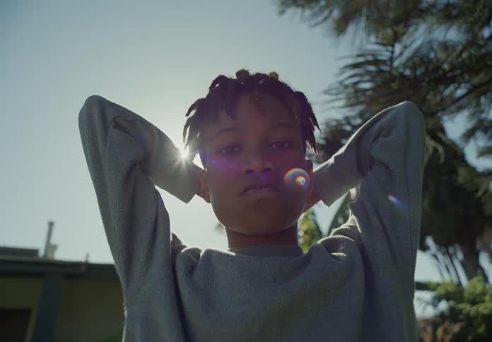 A close up of a boy standing outside with his arms behind his head