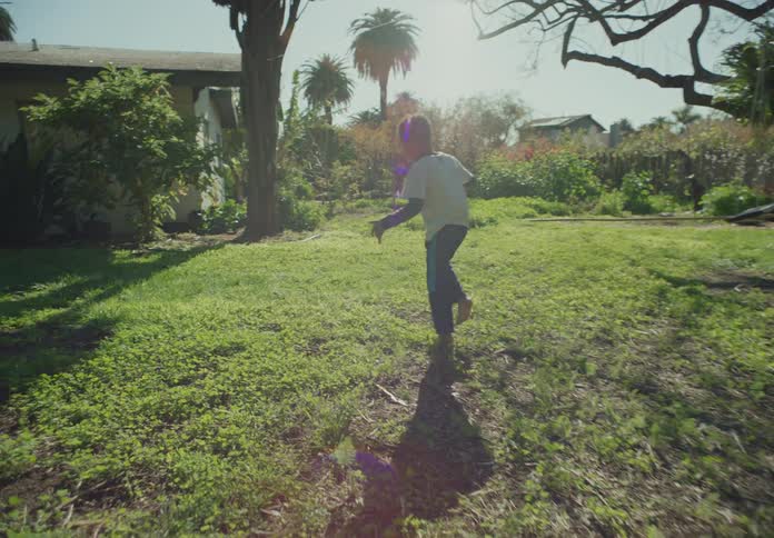 A boy walks barefoot on the grass in the backyard on a sunny day