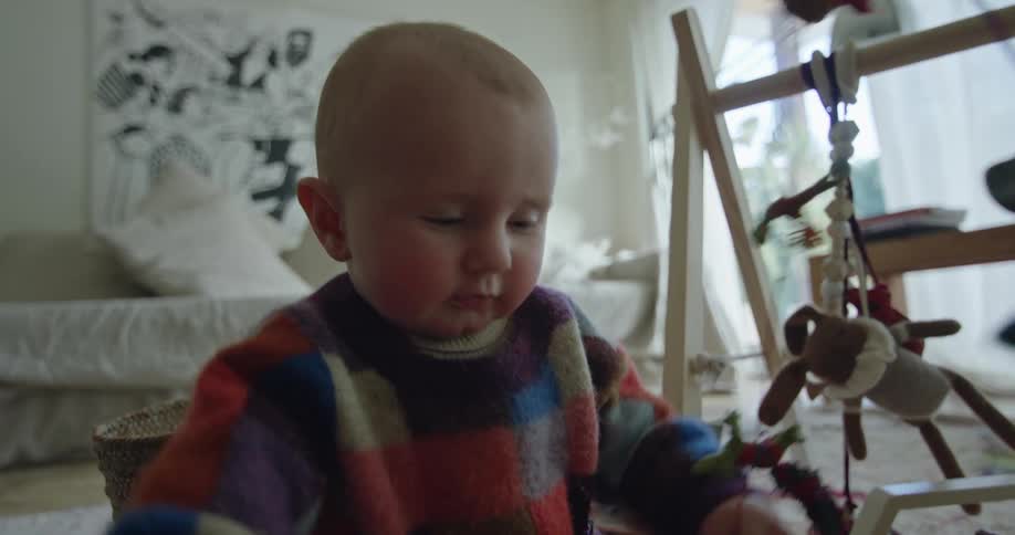 Baby sitting on the floor of the bedroom playing with hanging toys