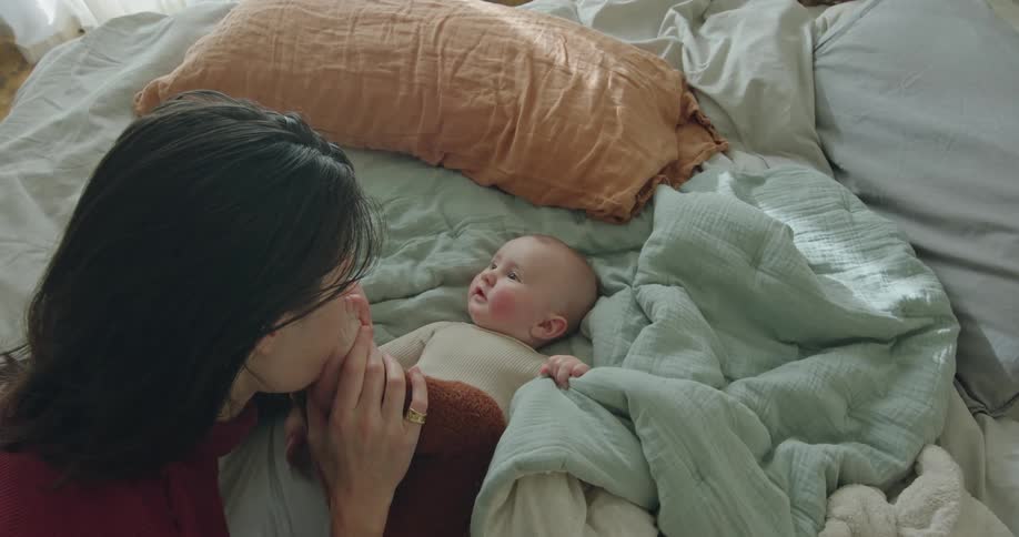 A woman kisses the feet of a baby resting on a bed during the day