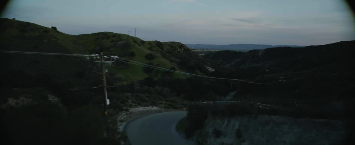 A black automobile with the headlights on travels fast on a winding mountain road as other traffic moves slow