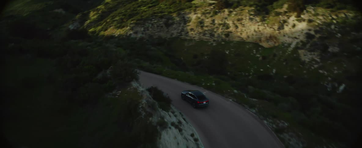 A black car travels on a winding forested mountain road