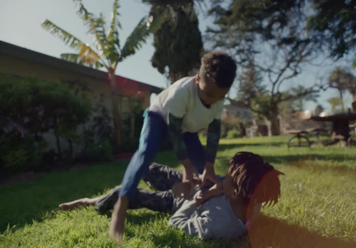 Siblings roughhousing and tumble playing energetically in the backyard at morning