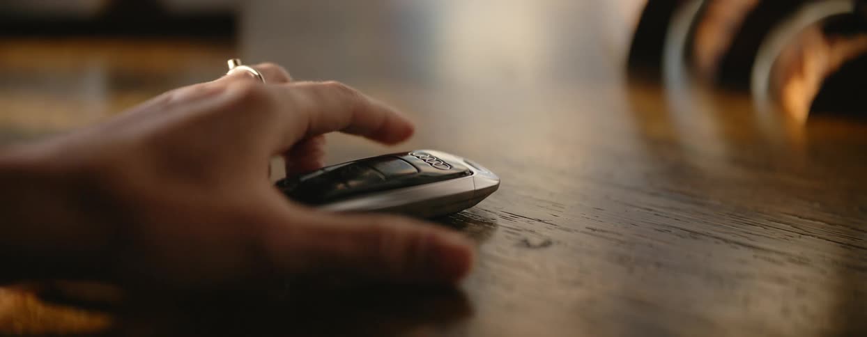 A car remote on a wooden table as a woman grabs it off the table
