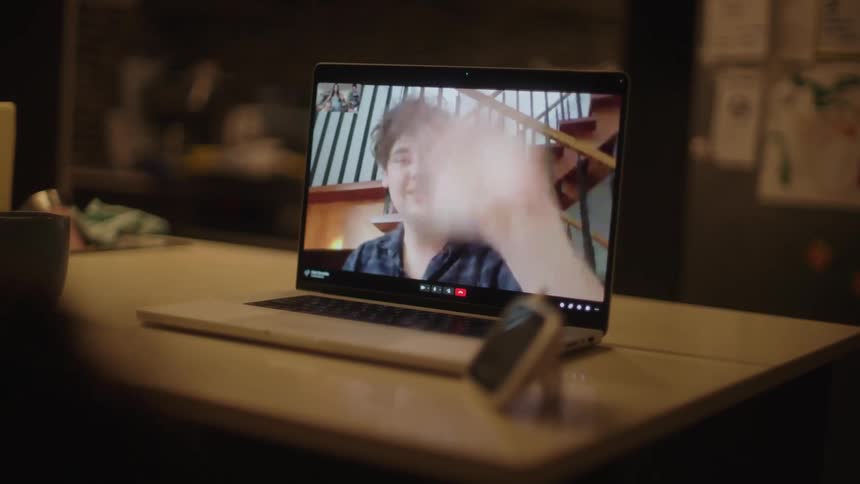 Two young men having a face time or zoom meeting on laptop waving and smiling at a dining table at nighttime