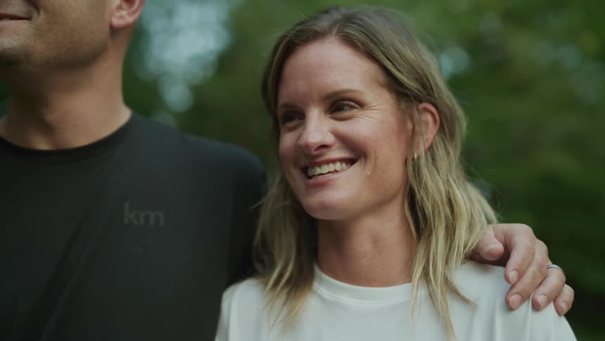 Close up of the face of a young woman talking and smile while his husband has an arm around her shoulder