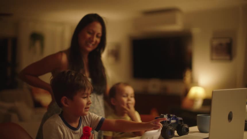 A mother standing behind her two songs sitting at their table in front of a laptop
