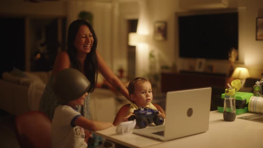 Happy family gathered on the living room smile and laugh at someone on a video call through a laptop