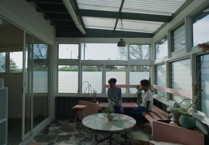 Two black boys sit on a bench on the porch and talk
