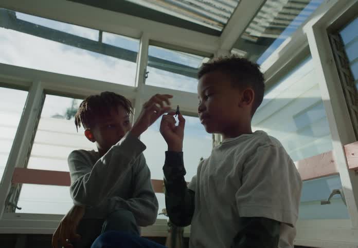Brothers sitting next to each otherin a sun room looking at something up close in the younger boys hand